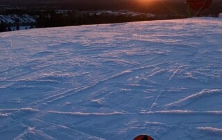 Photograph taken from the top of Pine Knob Ski and Snowboard resort shows the tips of two skis that the photographer is wearing and they are on top of the snowy hill, looking at the sun set on the horizon.
